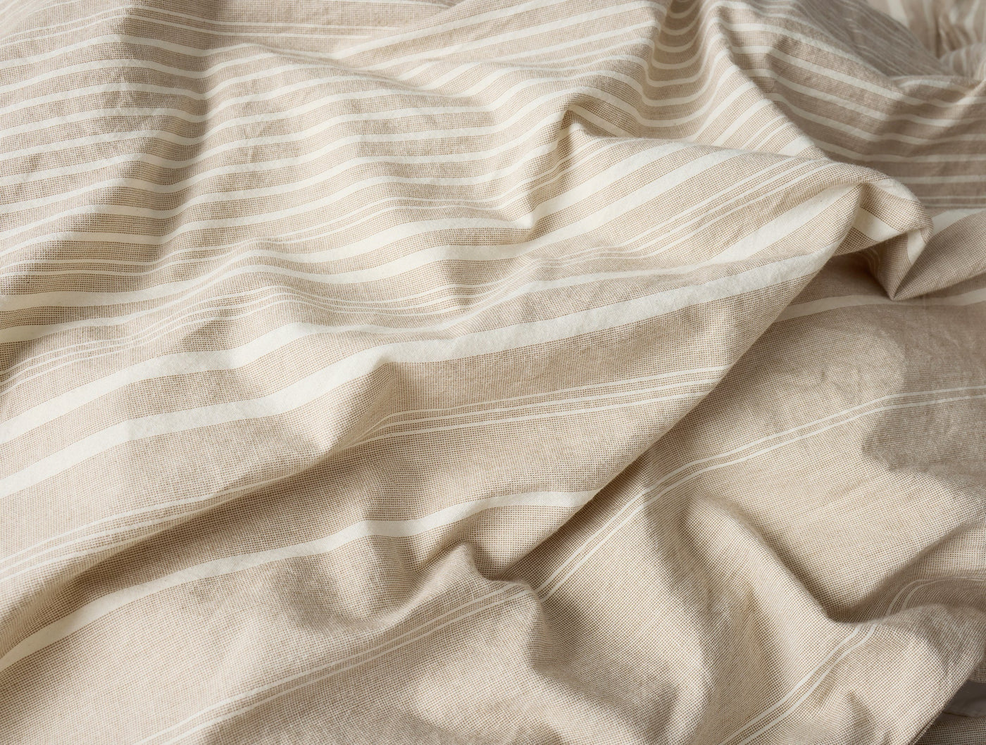 Close-up of draped Coyuchi Little Sur Stripe duvet in natural linen with ivory woven stripes.