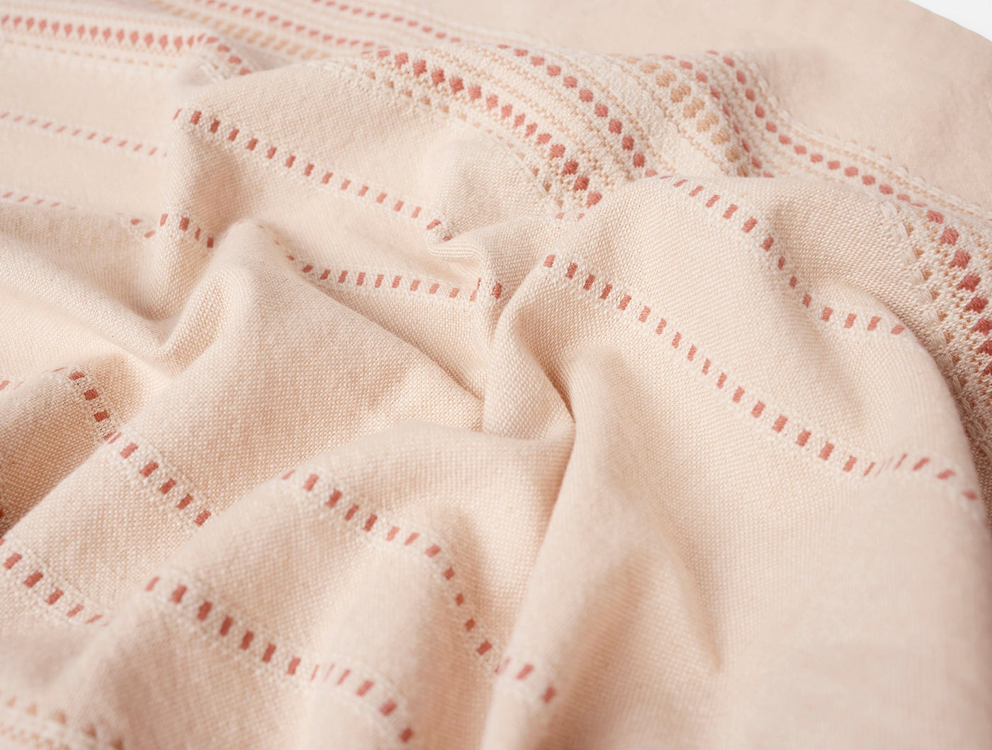 Close-up of Coyuchi Lobos napkin in blush, showing red dotted stitch grid pattern on soft knit fabric.