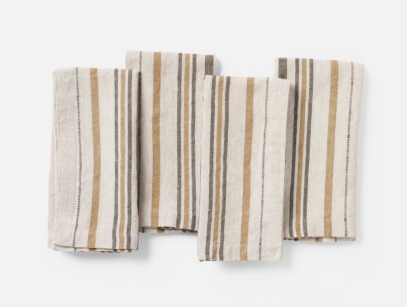 Four Coyuchi Mojave Linen napkins fanned flat, showing ochre and slate multi-stripe weave.