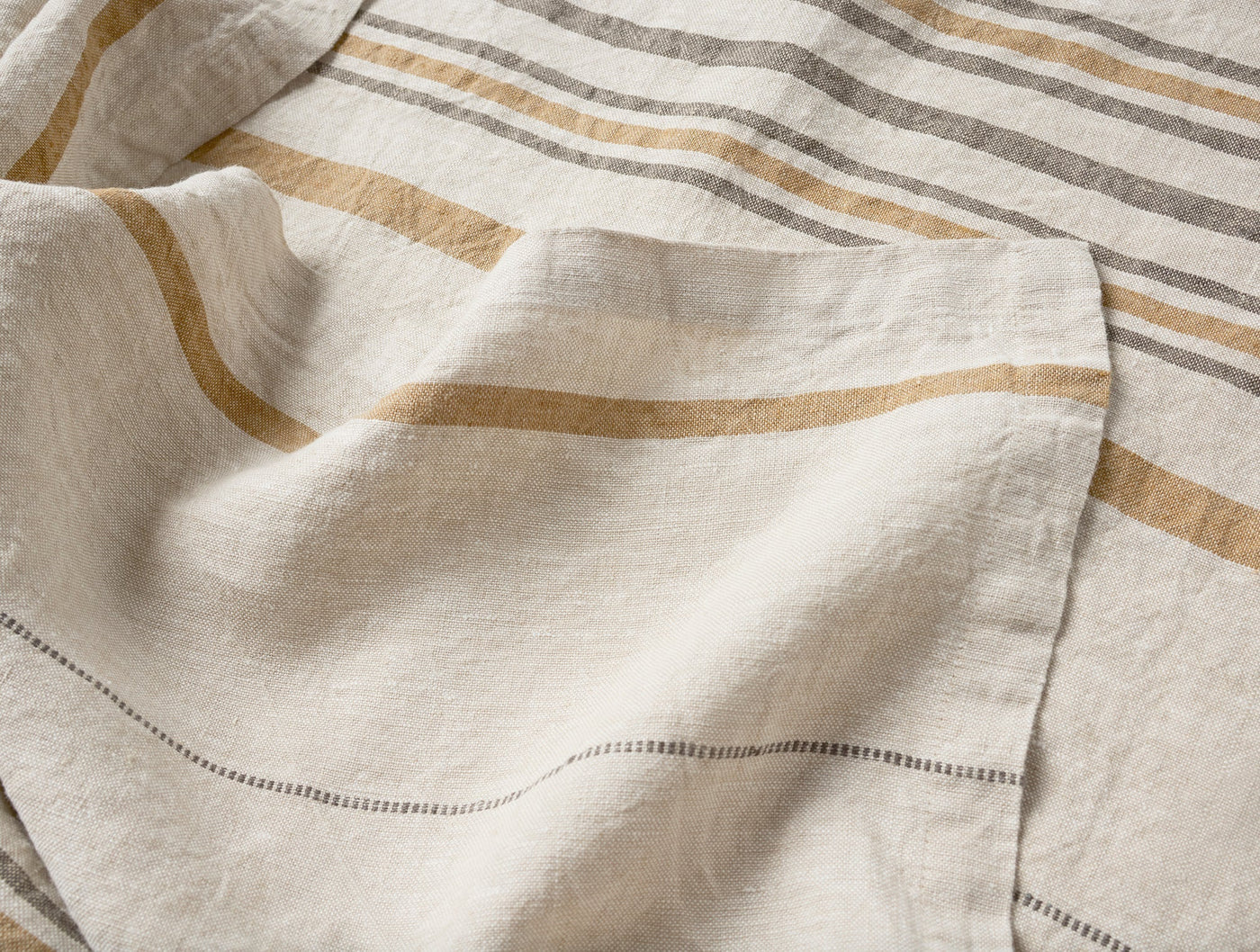 Close-up of Coyuchi Mojave Linen Throw hemstitch detail with gold and gray stripes.