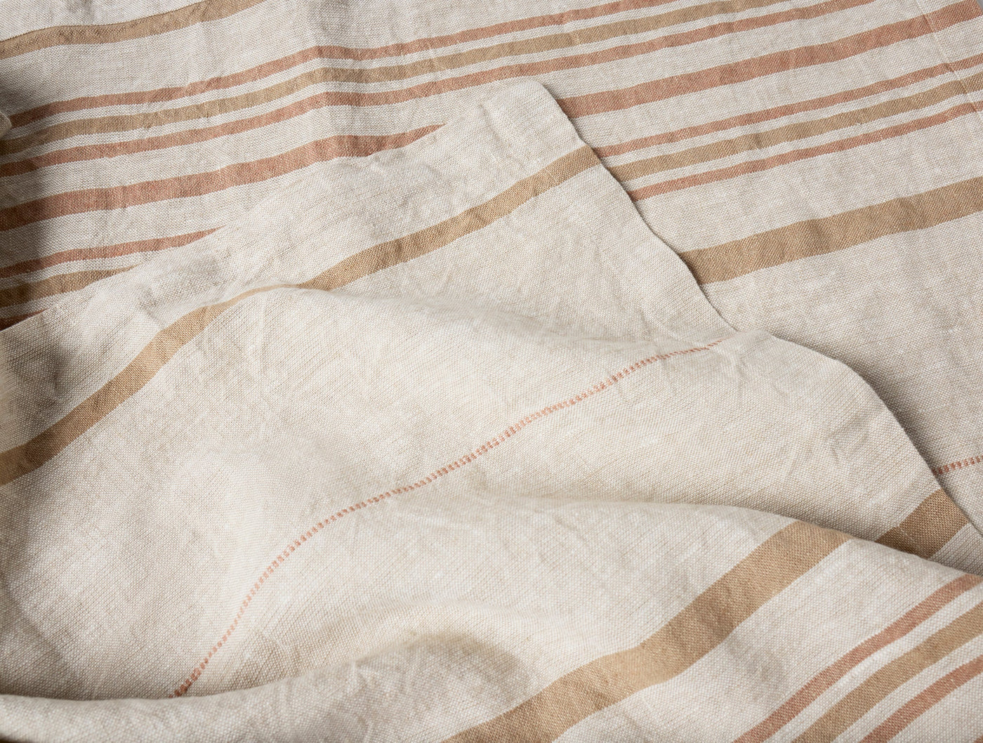 Close-up of ivory linen throw with terracotta and tan stripes, hemstitch detail visible.