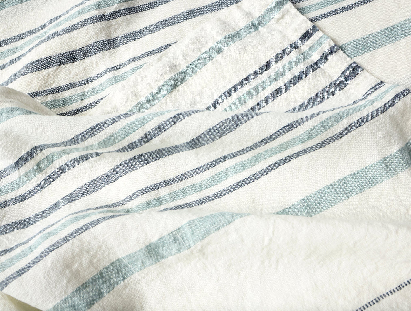 Close-up of Coyuchi Mojave Linen throw showing ivory fabric with blue and sage stripe detail.
