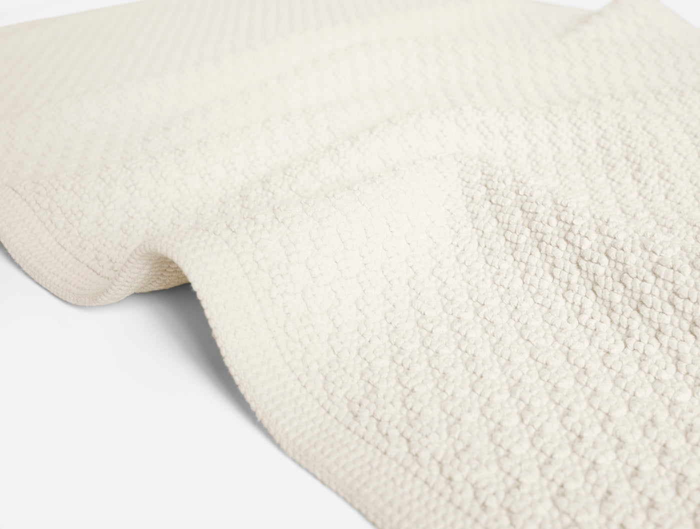 Close-up of ivory Coyuchi Moonstone bath rug showing nubby woven texture and folded edge.