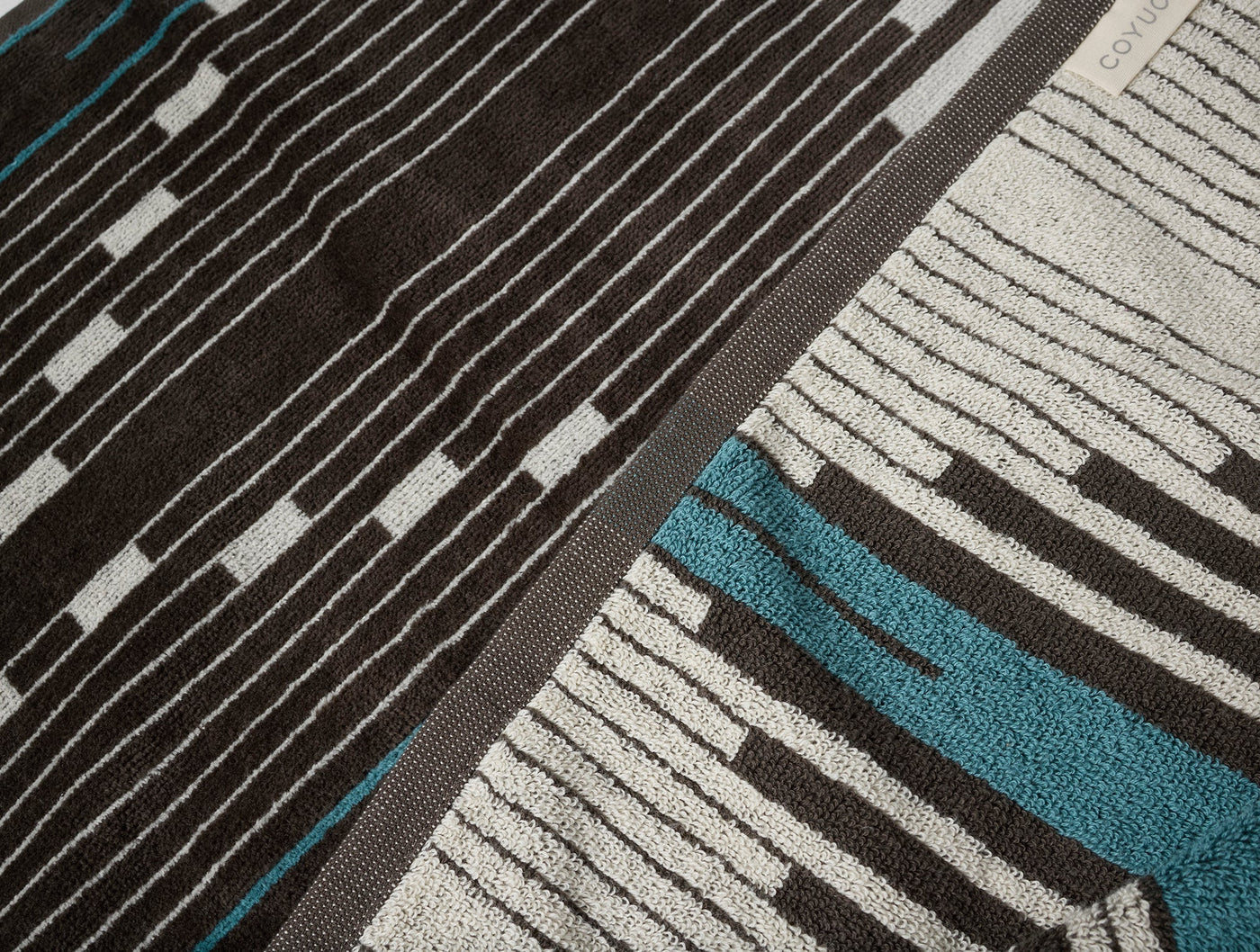 Close-up of Coyuchi Morelia beach towel showing charcoal and teal stripe pattern with textured weave.