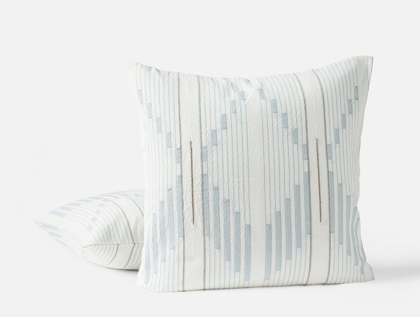 Two Coyuchi Morelia pillows, ivory with pale blue geometric stripe pattern, angled view.