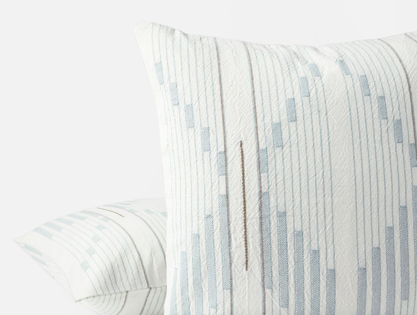 Close-up of Coyuchi Morelia pillow corner, ivory with pale blue geometric embroidery and stripe texture.