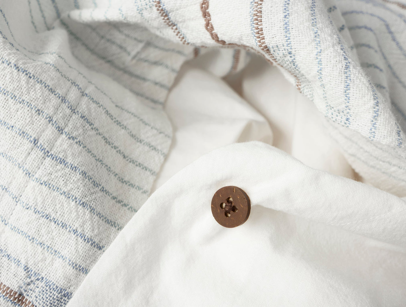 Close-up of walnut button closure on white Coyuchi Morelia duvet cover with striped linen.