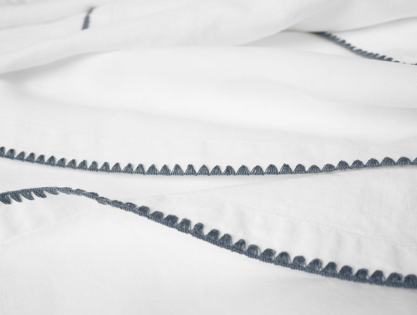 Close-up of white linen with slate blue scalloped embroidered trim detail.
