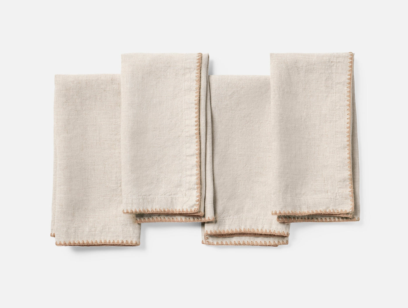 Four natural linen cocktail napkins with tan embroidered picot edge trim, folded flat.