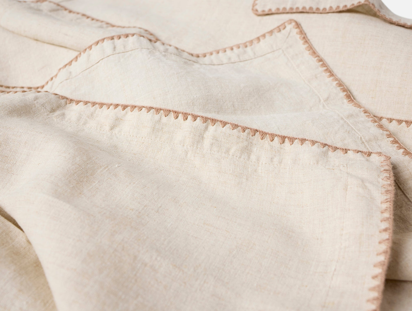 Close-up of ivory linen napkins with terracotta blanket-stitch embroidered edges, stacked and draped.