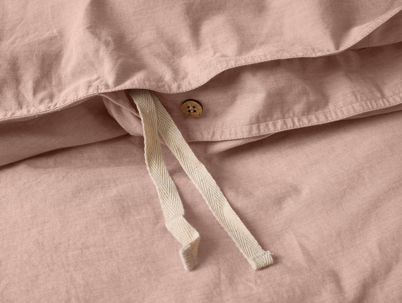 Close-up of Coyuchi duvet cover interior showing wood button closure and ivory cotton ties on blush percale.