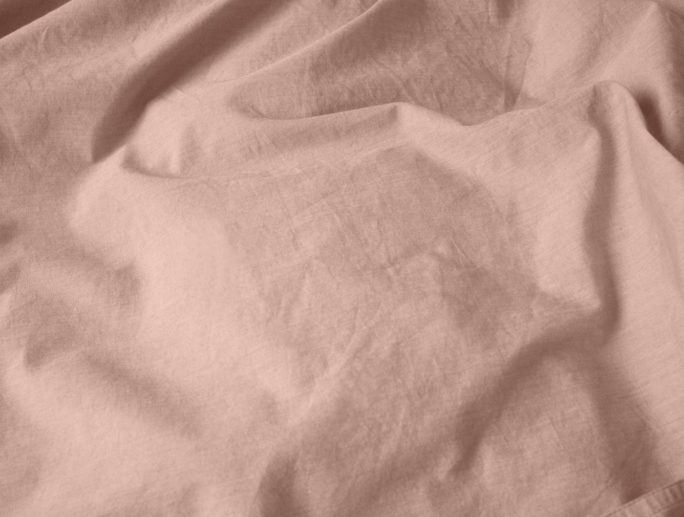 Close-up of blush Coyuchi Crinkled Percale duvet cover showing relaxed, natural wrinkled texture.