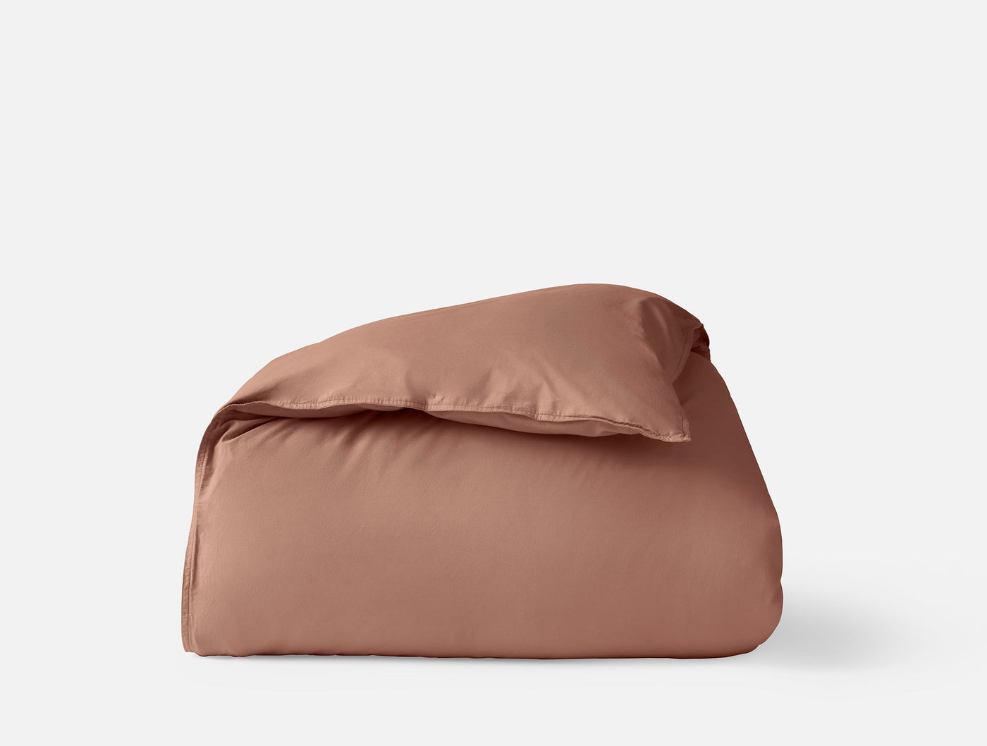 Coyuchi Crinkled Percale duvet cover in terracotta, folded with pillow on white background.