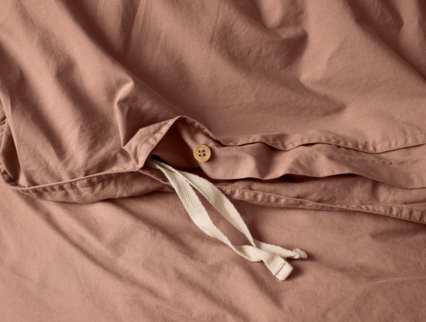 Close-up of Coyuchi Crinkled Percale duvet cover closure with wooden button and ivory ties.