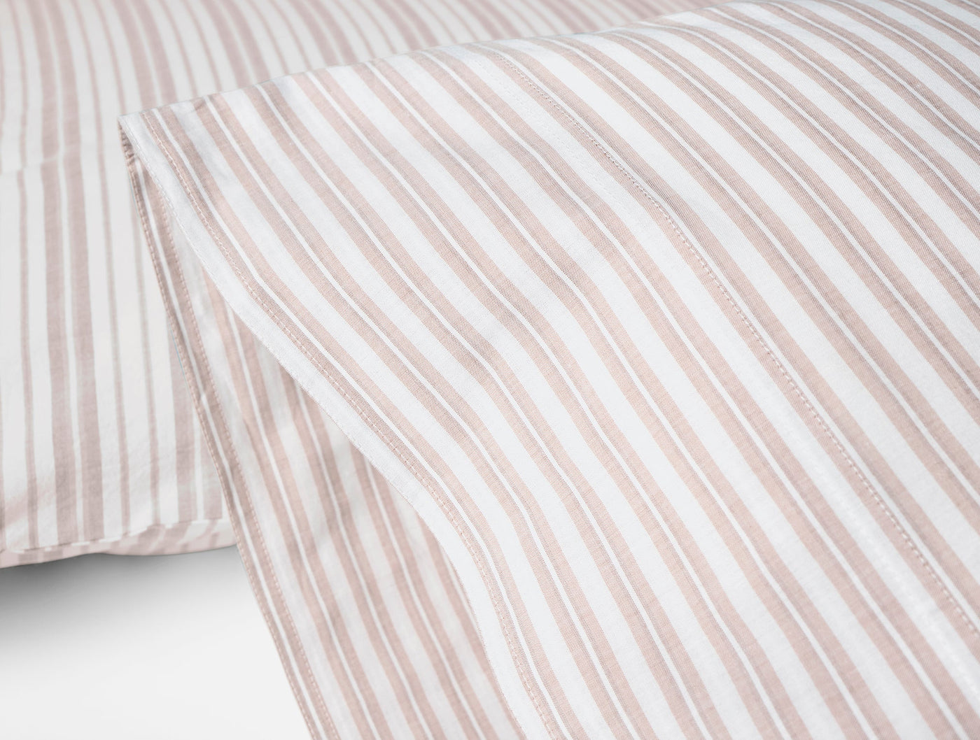 Close-up of Coyuchi Crinkled Percale pillowcases showing blush and white ticking stripes.
