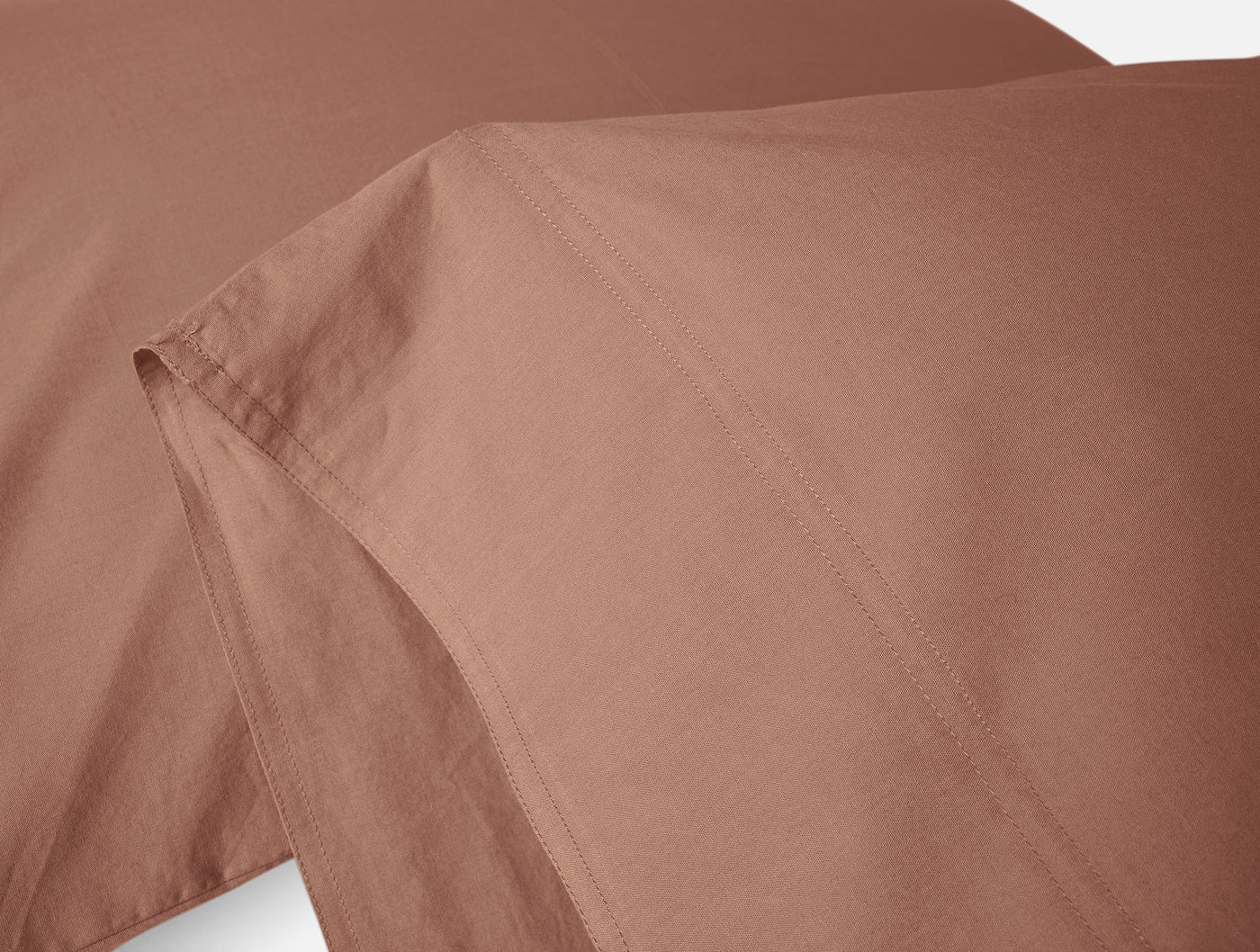 Close-up of Coyuchi Crinkled Percale sheet set hem detail in terracotta.