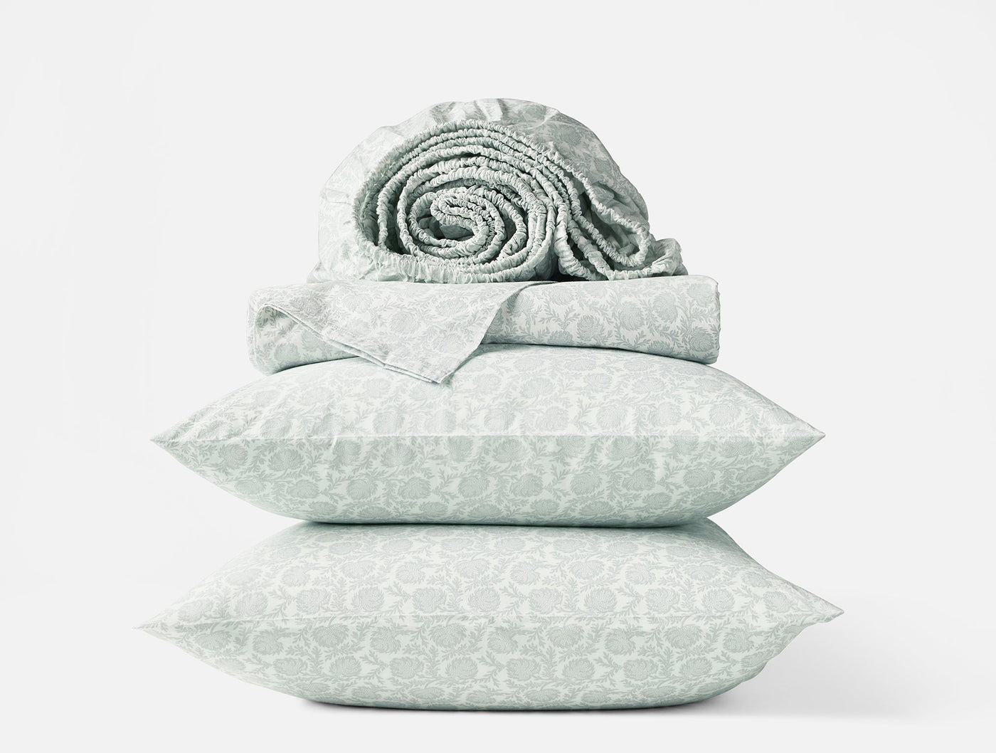 Coyuchi Print Percale sheet set in sage, stacked pillowcases with rolled sheets on top.