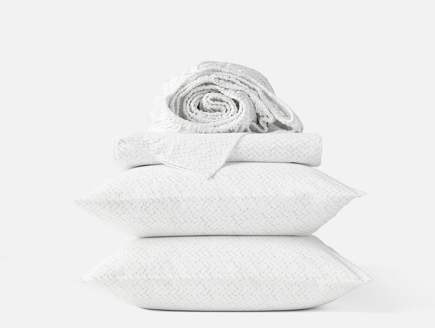 Rolled sheet atop folded pillowcases in white chevron percale, stacked against light background.