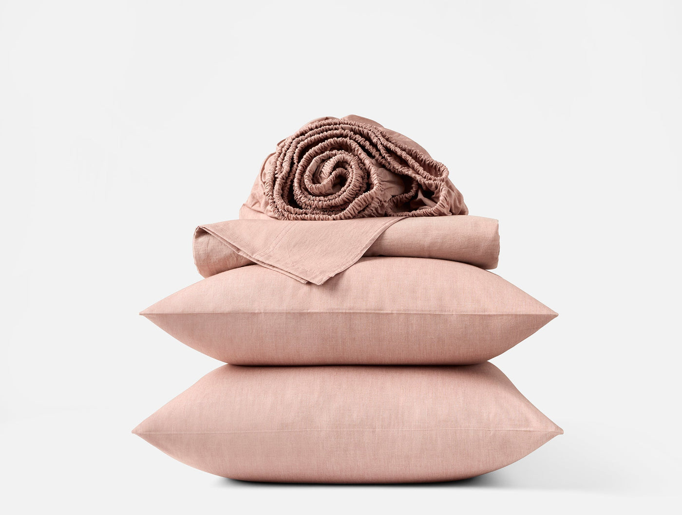 Blush pink crinkled percale sheet set folded and stacked with matching pillows and a rolled blanket.