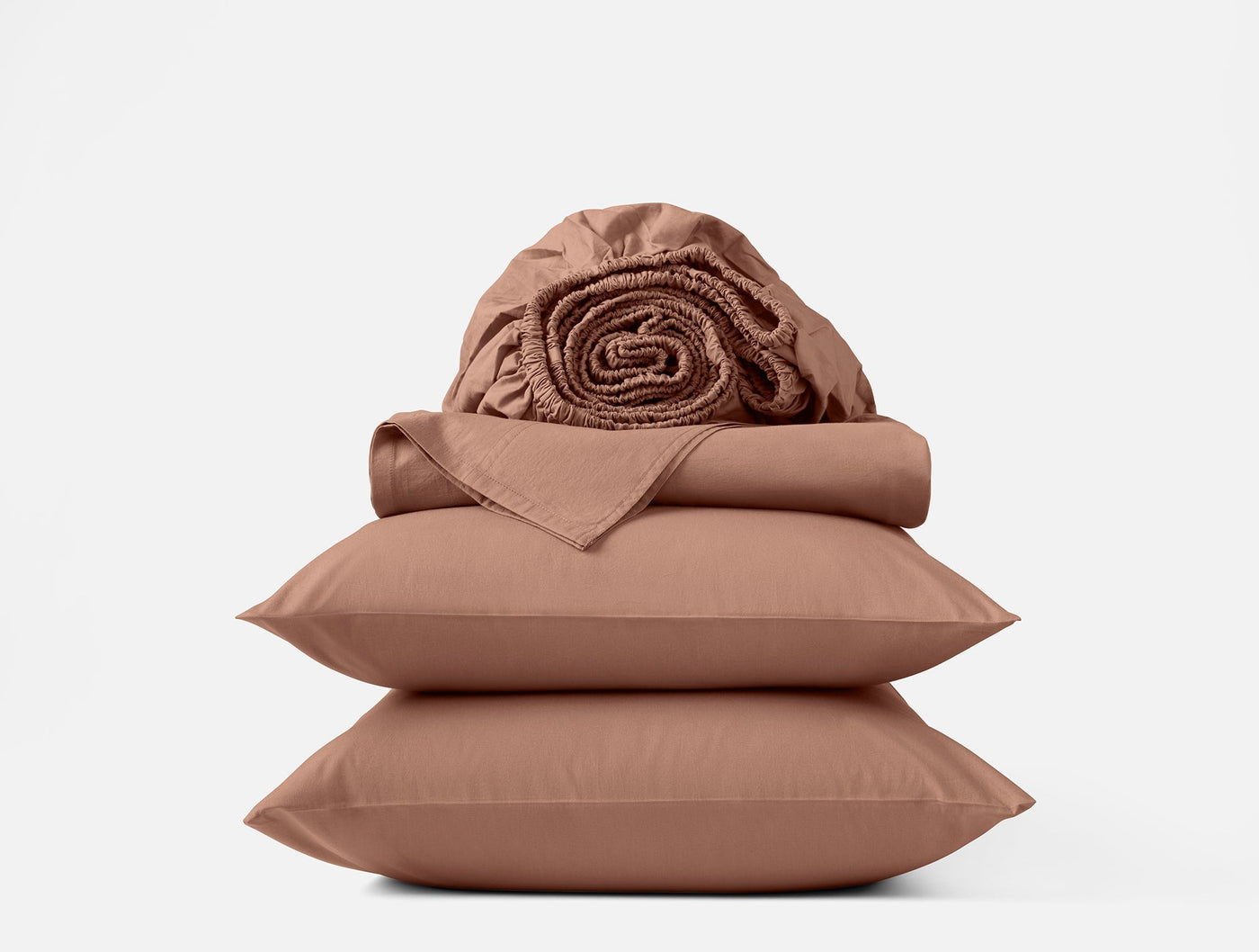 Stacked Coyuchi Crinkled Percale sheet set in terracotta, folded flat sheets and two pillowcases with rolled fitted sheet on top.