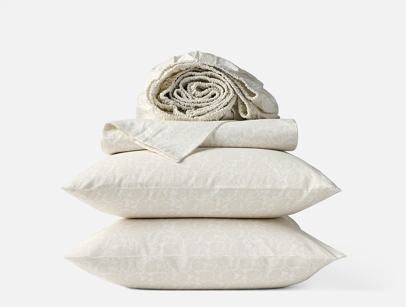 Stacked ivory percale pillowcases with subtle print, flat sheet, and rolled fitted sheet above.