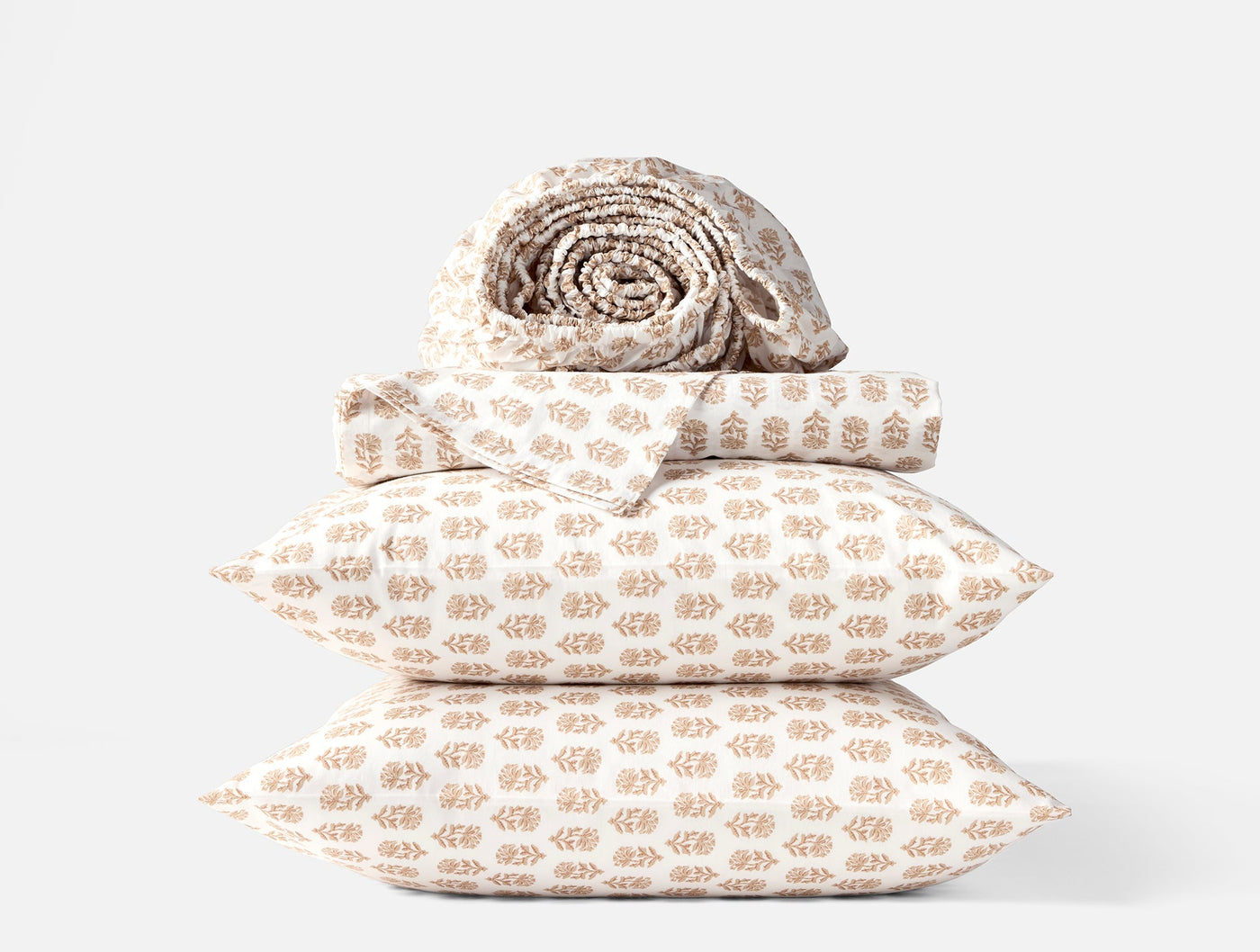 Coyuchi Print Percale sheet set in tan leaf block print, stacked with rolled sheet on top.