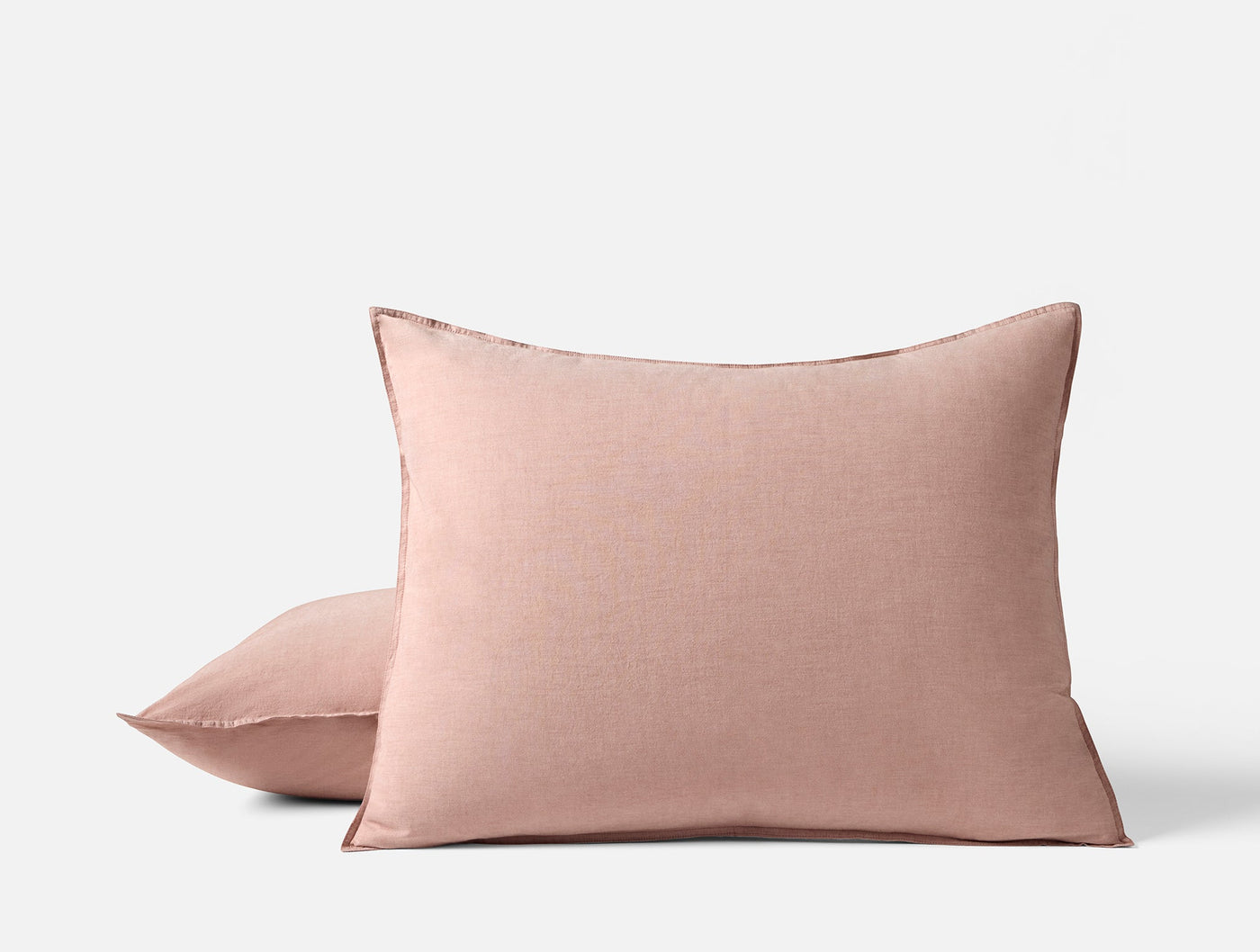 Close-up of two blush Coyuchi Crinkled Percale pillow shams stacked on white background.