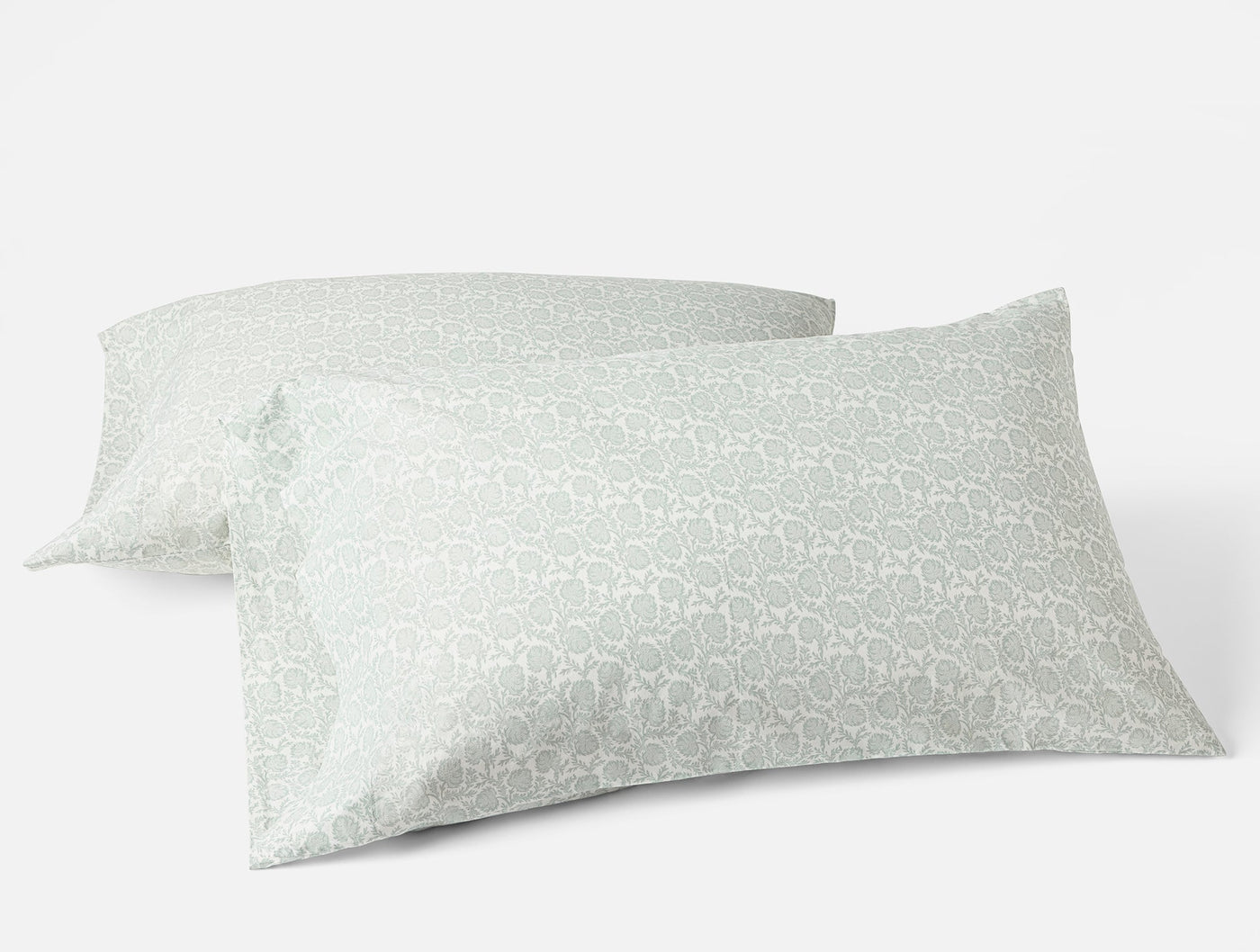 Two Coyuchi Print Percale pillowcases in sage green geometric pattern, angled view.
