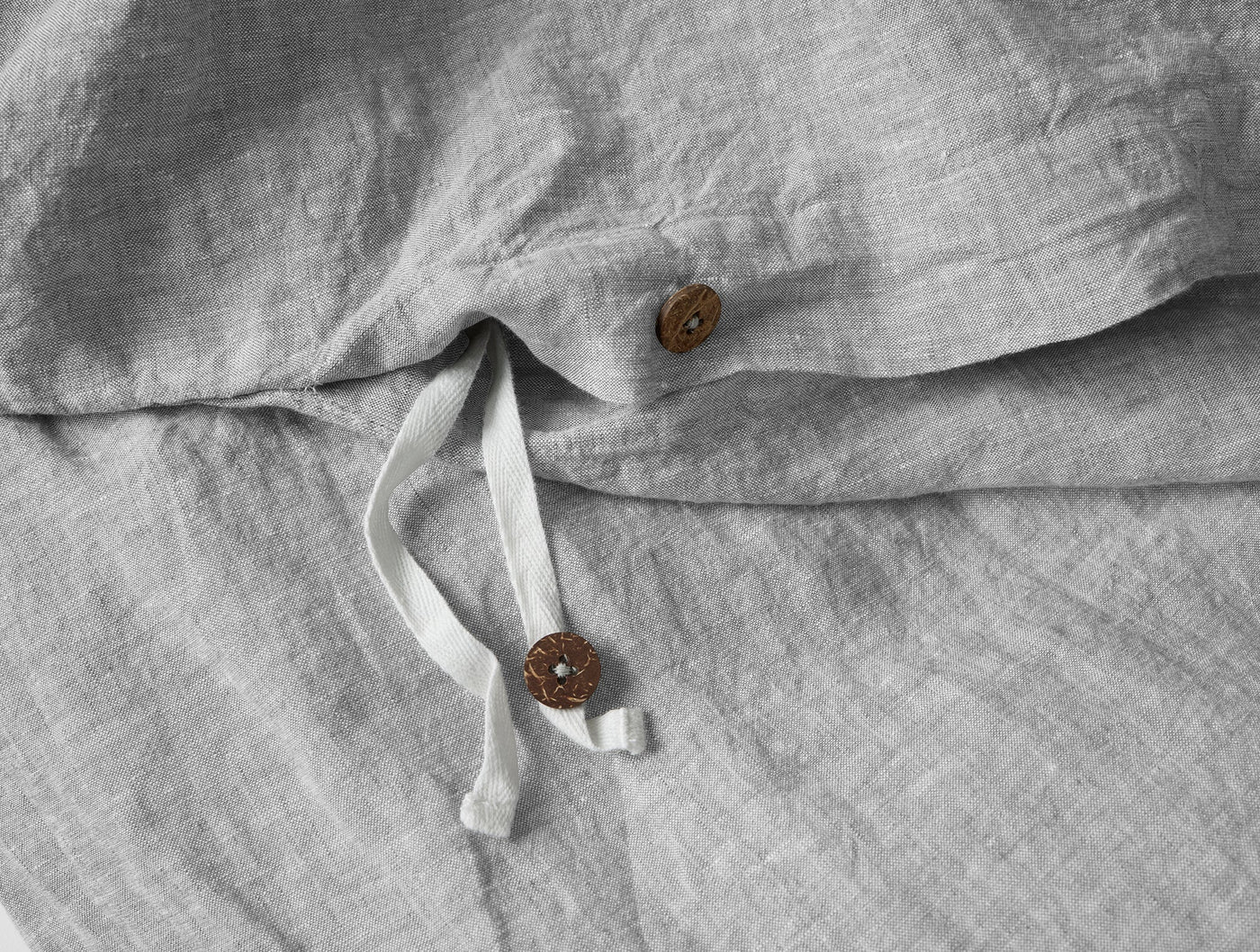 Close-up of mist linen duvet cover with rattan buttons and tie closure detail.