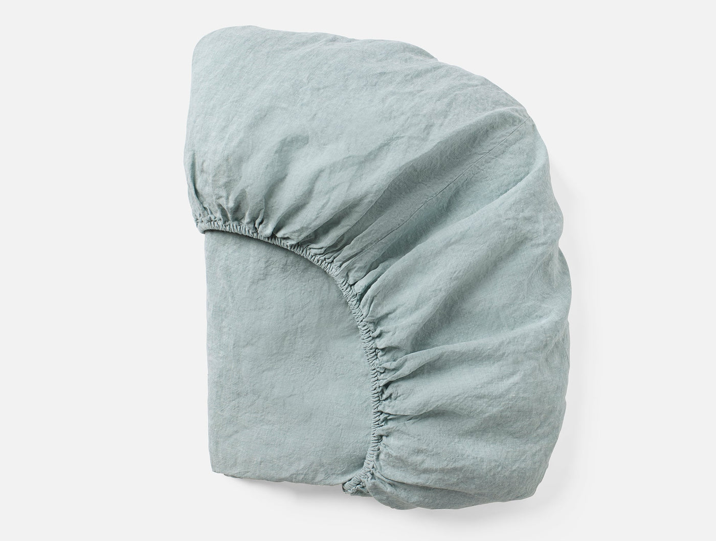 Sage green fitted sheet folded to show elasticized corner and relaxed linen texture.