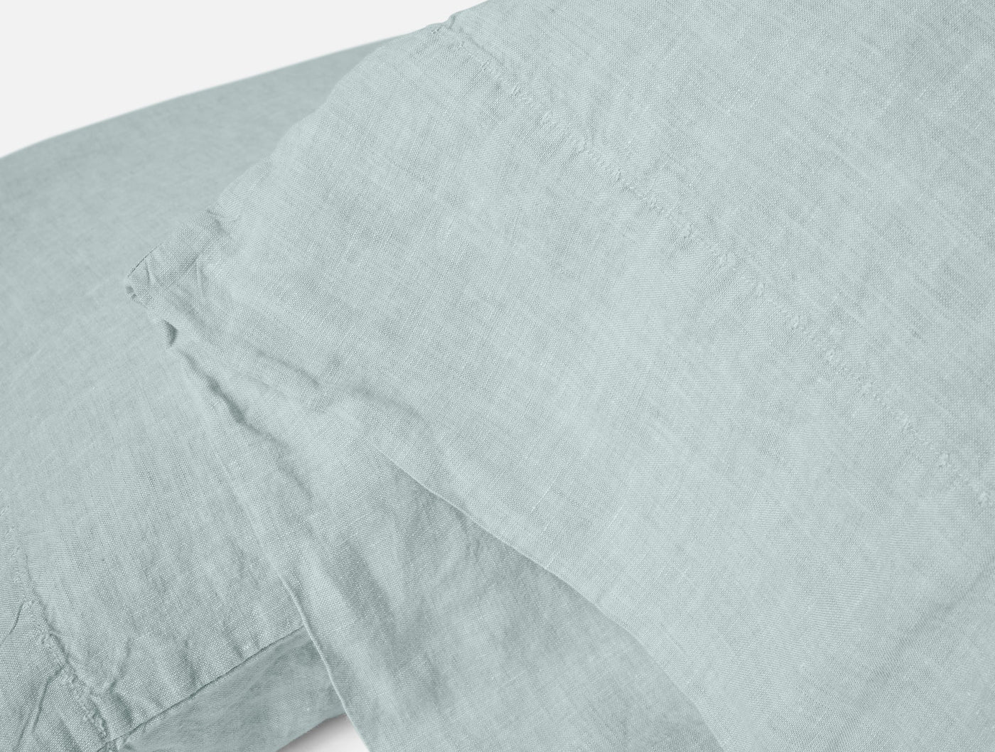 Close-up of pale seafoam Coyuchi Relaxed Linen pillowcase showing natural woven texture and hem detail.