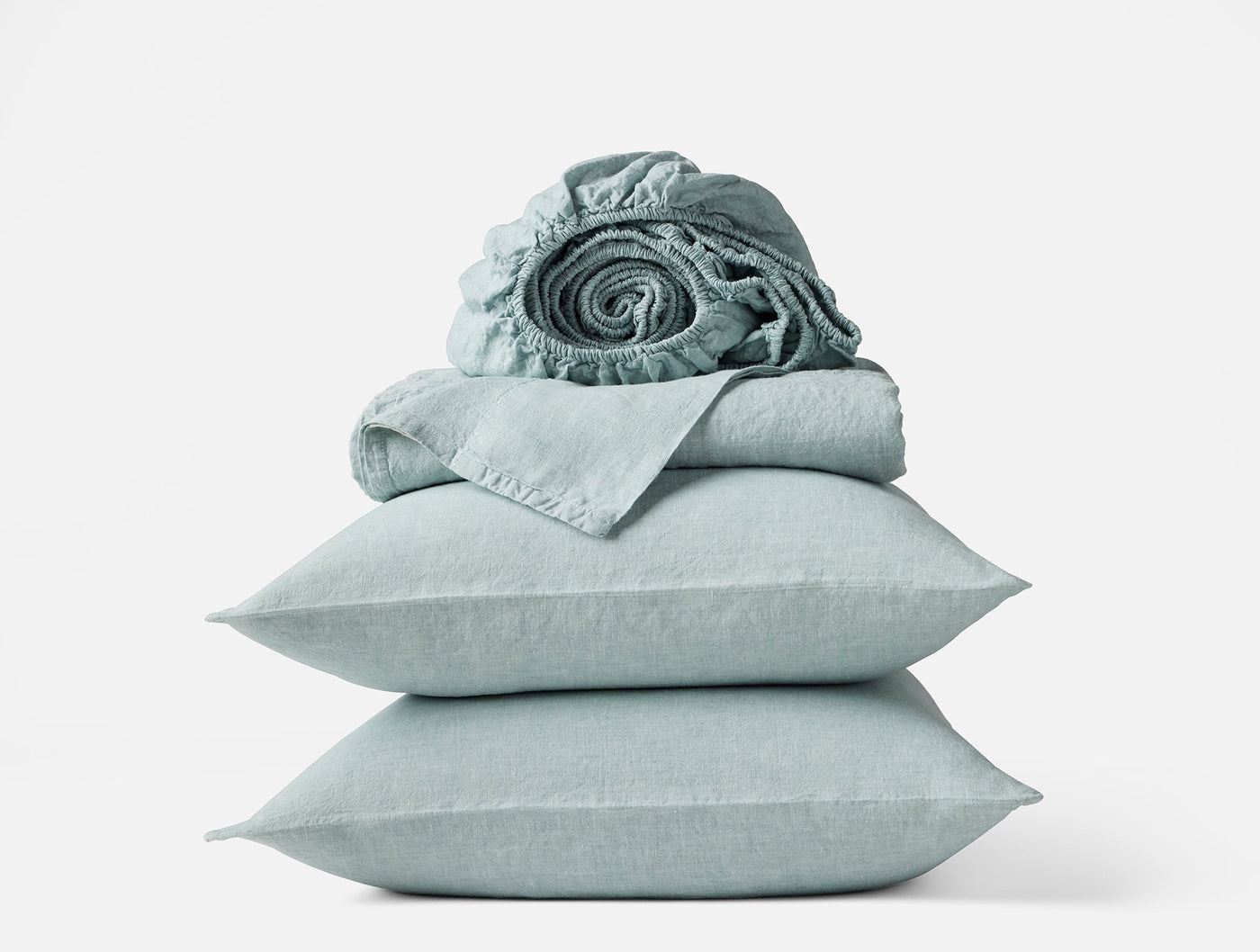 Coyuchi Relaxed Linen sheet set in sage, pillowcases stacked with rolled fitted sheet on top.