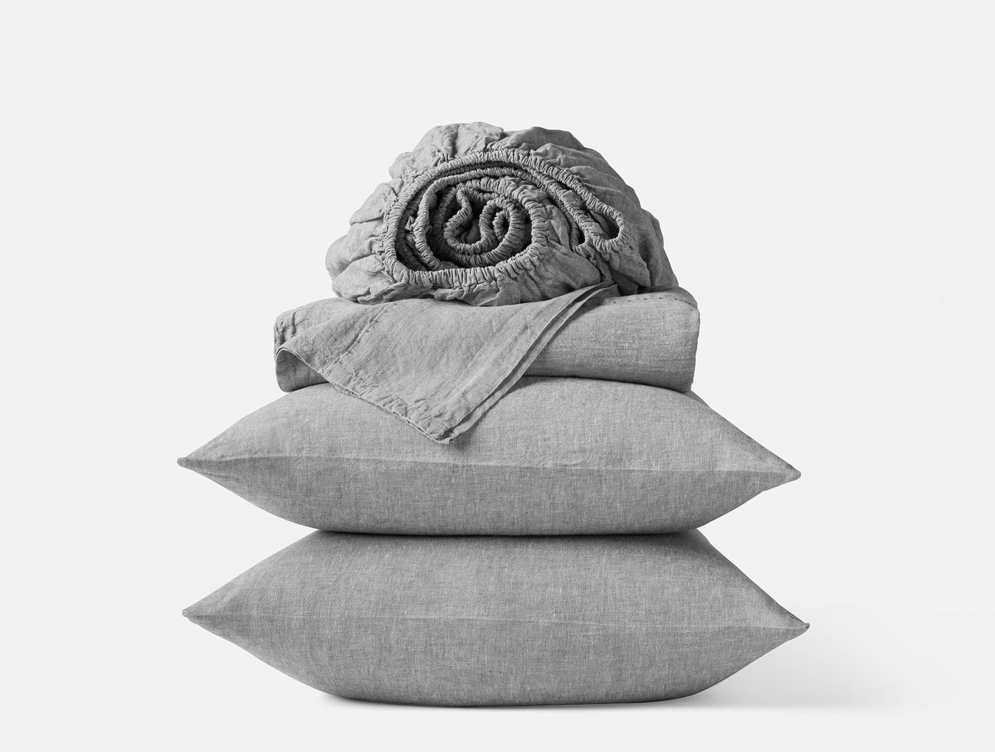 Stacked grey linen sheet set with two pillowcases and a rolled fitted sheet on top.