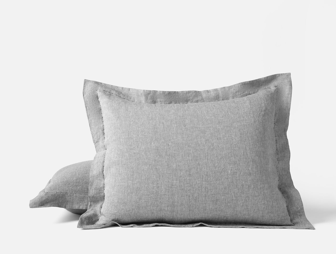 Stacked silver grey linen pillow shams with flanged edges on white background.