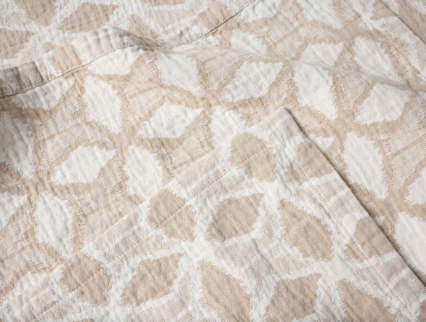 Close-up of Coyuchi Palomar blanket showing sand and white leaf pattern weave texture.