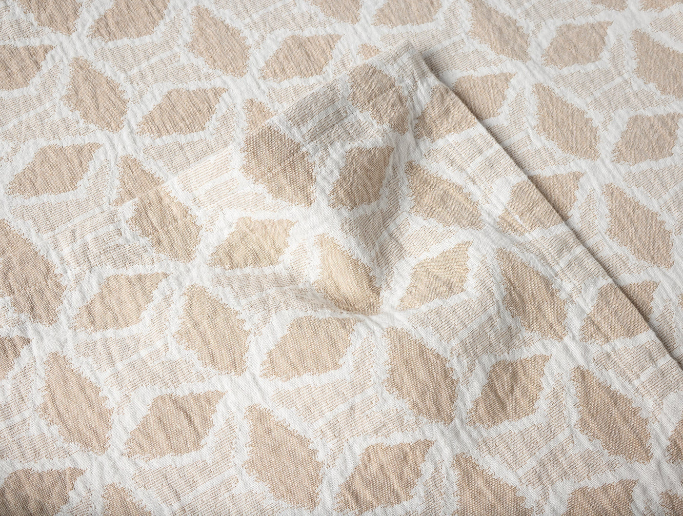 Close-up of Coyuchi Palomar blanket corner fold, sand and white geometric pattern.