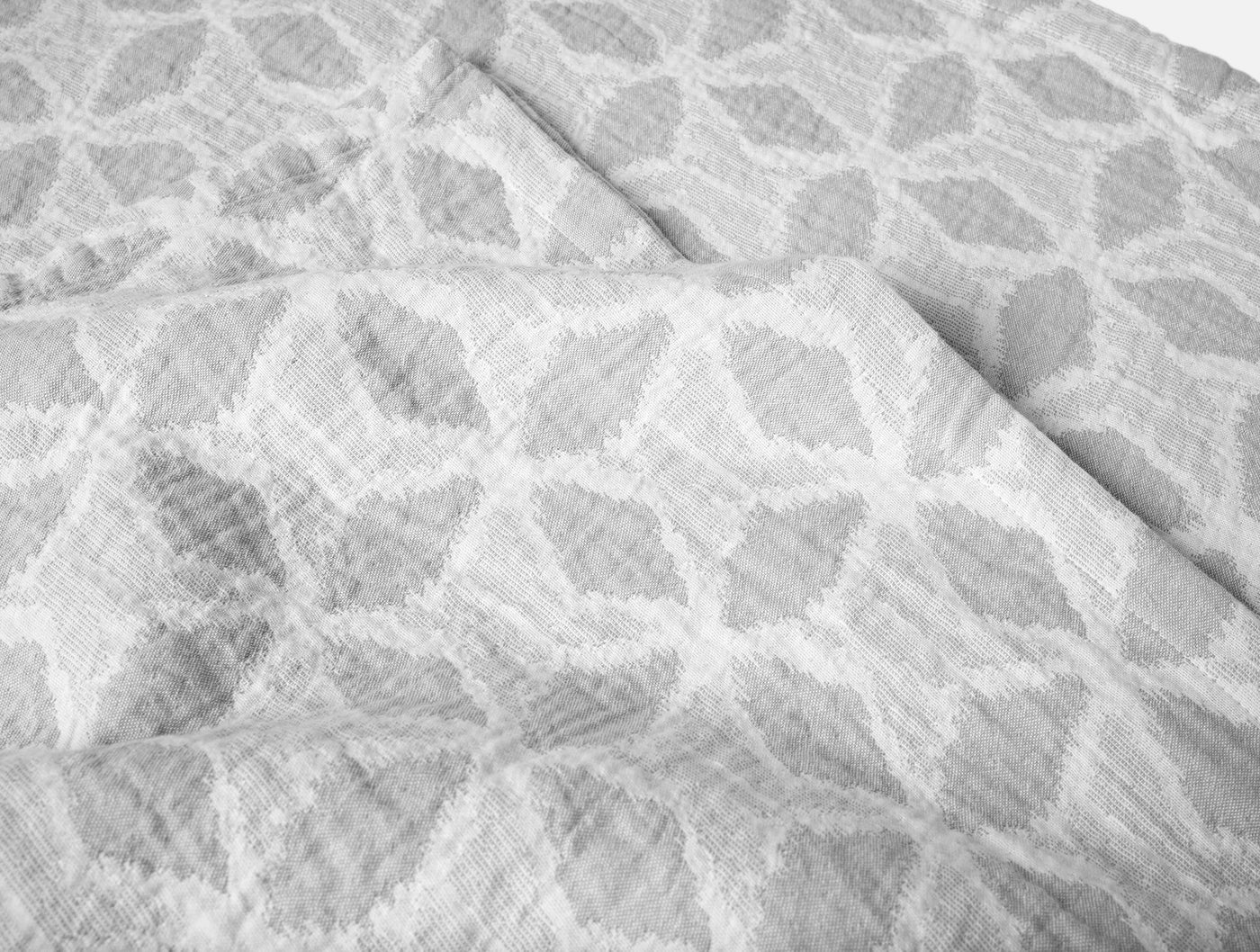 Close-up of Coyuchi Palomar blanket showing silver geometric leaf-pattern weave texture.