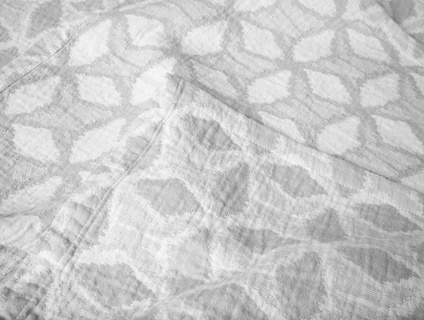 Close-up of Coyuchi Palomar blanket showing woven geometric floral pattern in white.
