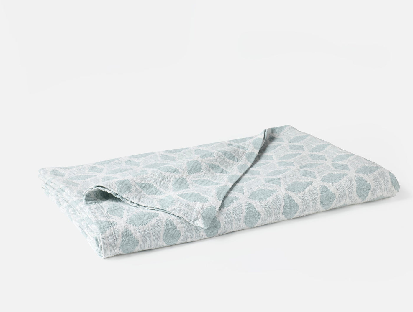Close-up of folded Coyuchi Palomar blanket in seafoam with organic leaf print.