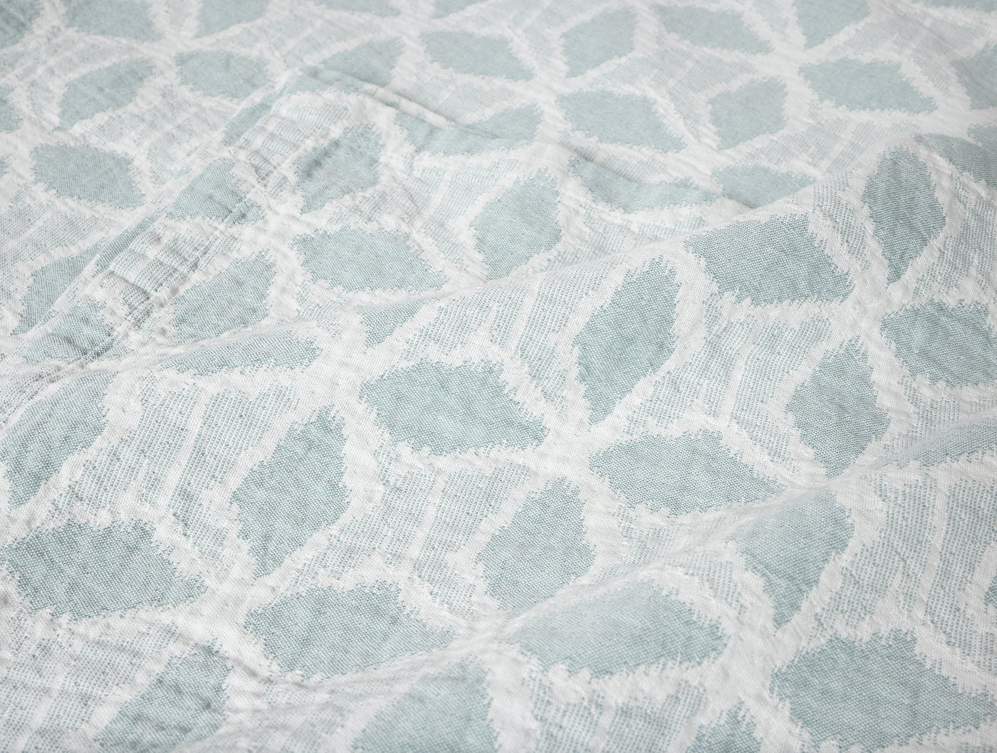 Close-up of Coyuchi Palomar blanket in seafoam, showing textured organic leaf pattern weave.