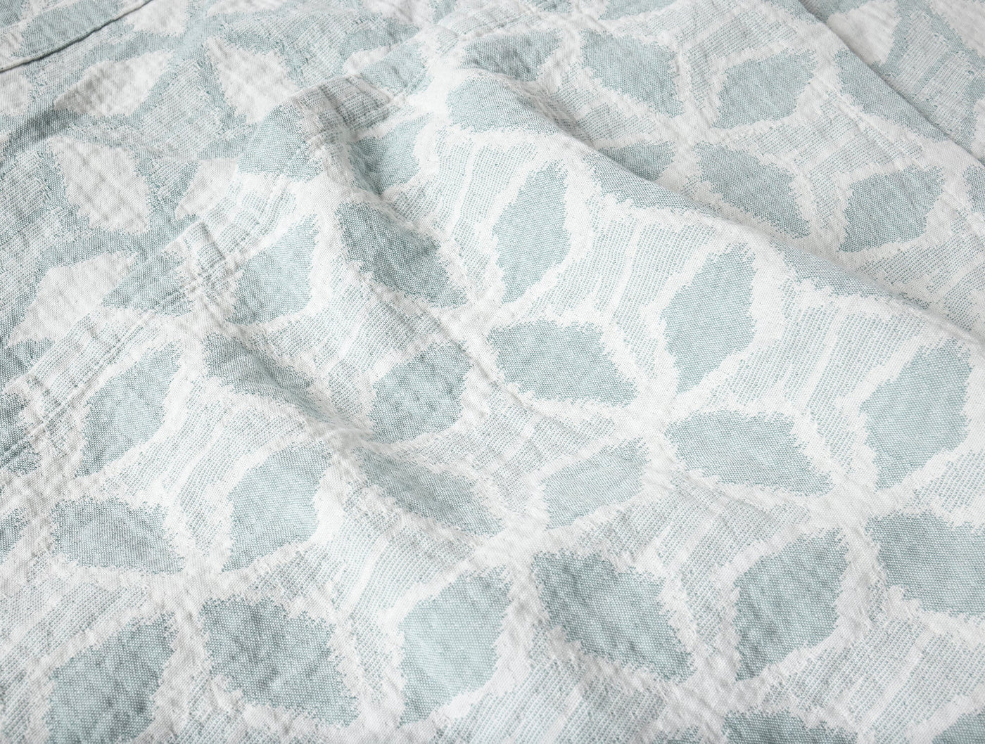 Close-up of Coyuchi Palomar blanket weave showing seafoam leaf pattern on white cotton.
