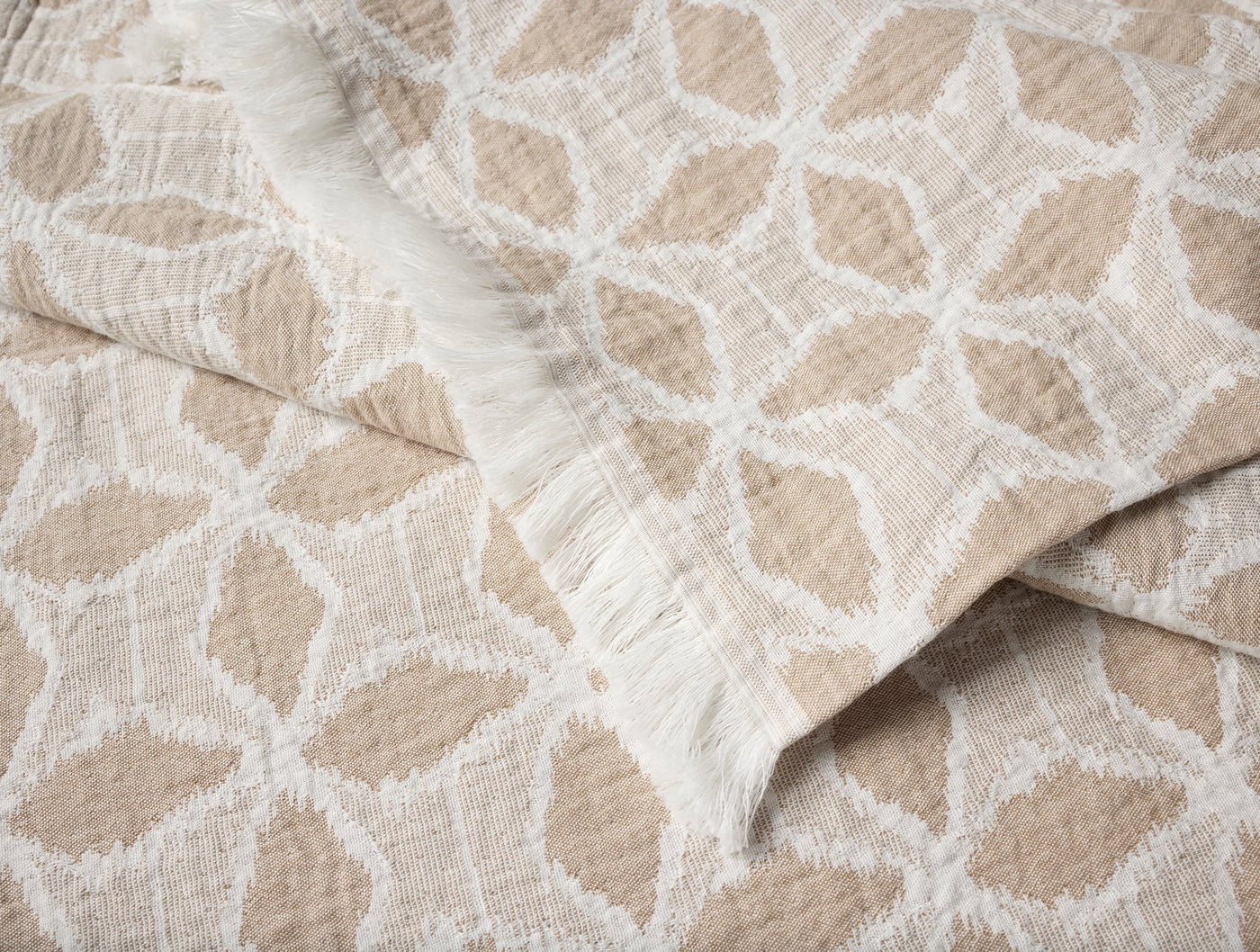 Close-up of Coyuchi Palomar throw in sand, showing geometric star pattern and fringe edge.