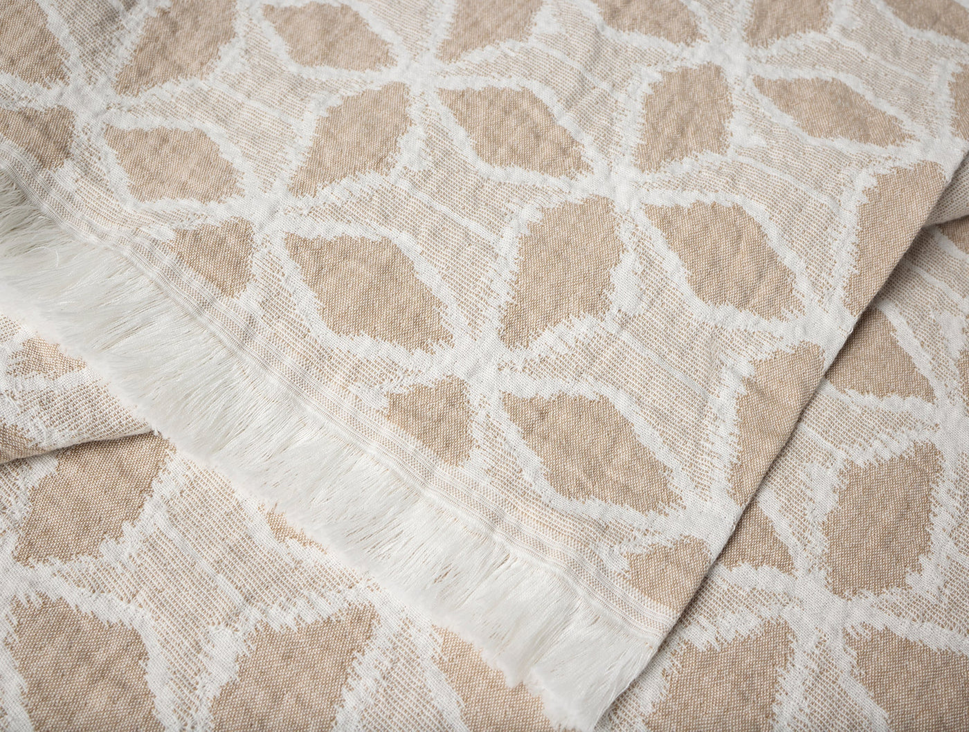 Close-up of Coyuchi Palomar throw fringe edge, sand and white geometric floral pattern.