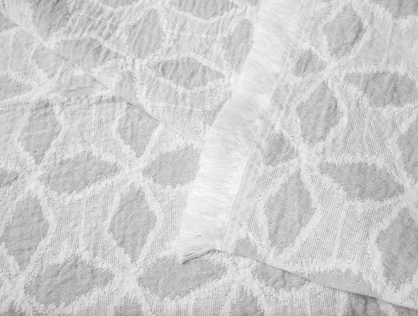 Close-up of Coyuchi Palomar throw in white, showing textured ogee jacquard weave and fringe edge detail.