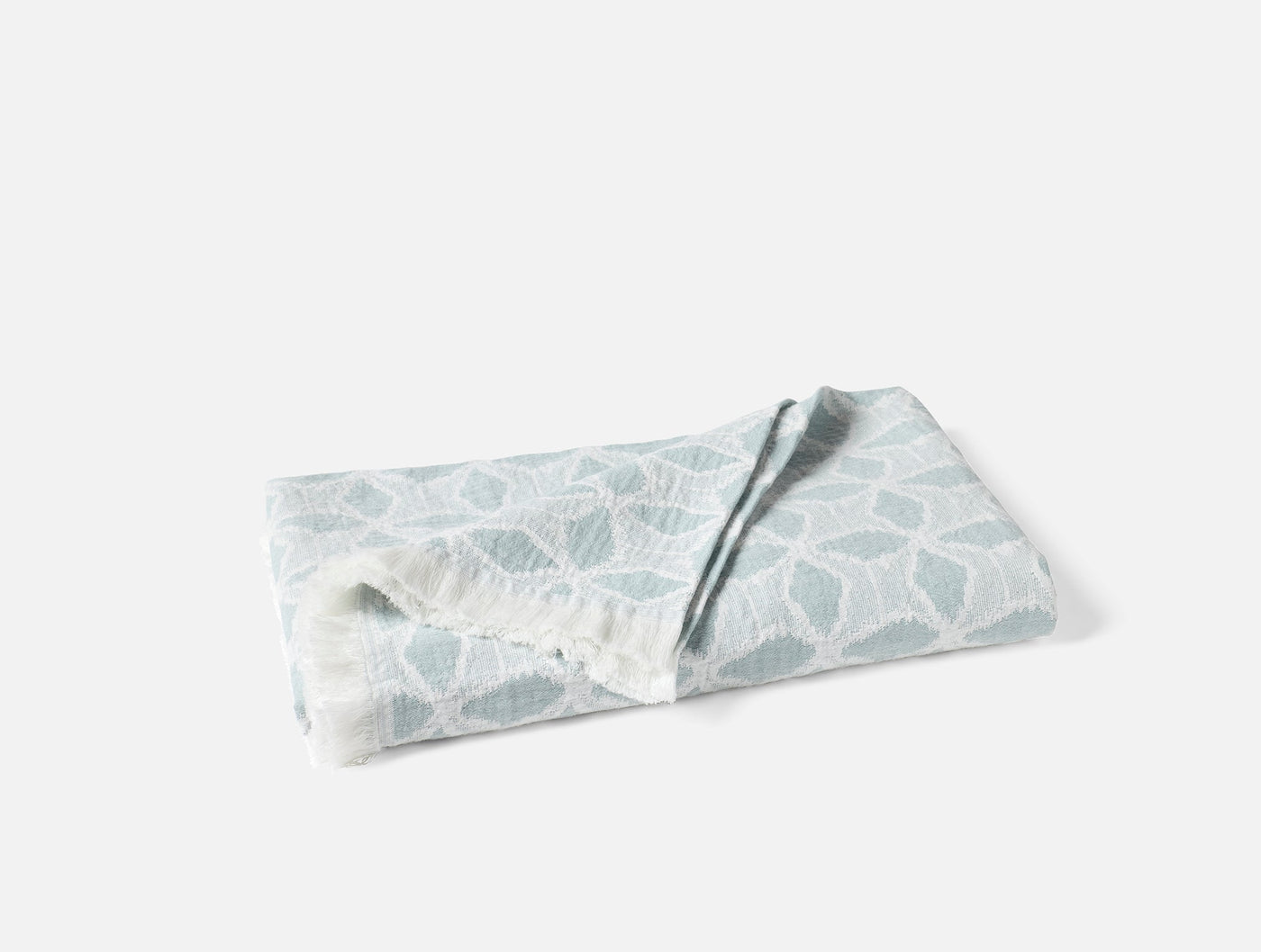 Folded Coyuchi Palomar throw showing seafoam geometric leaf jacquard pattern and fringe edge.