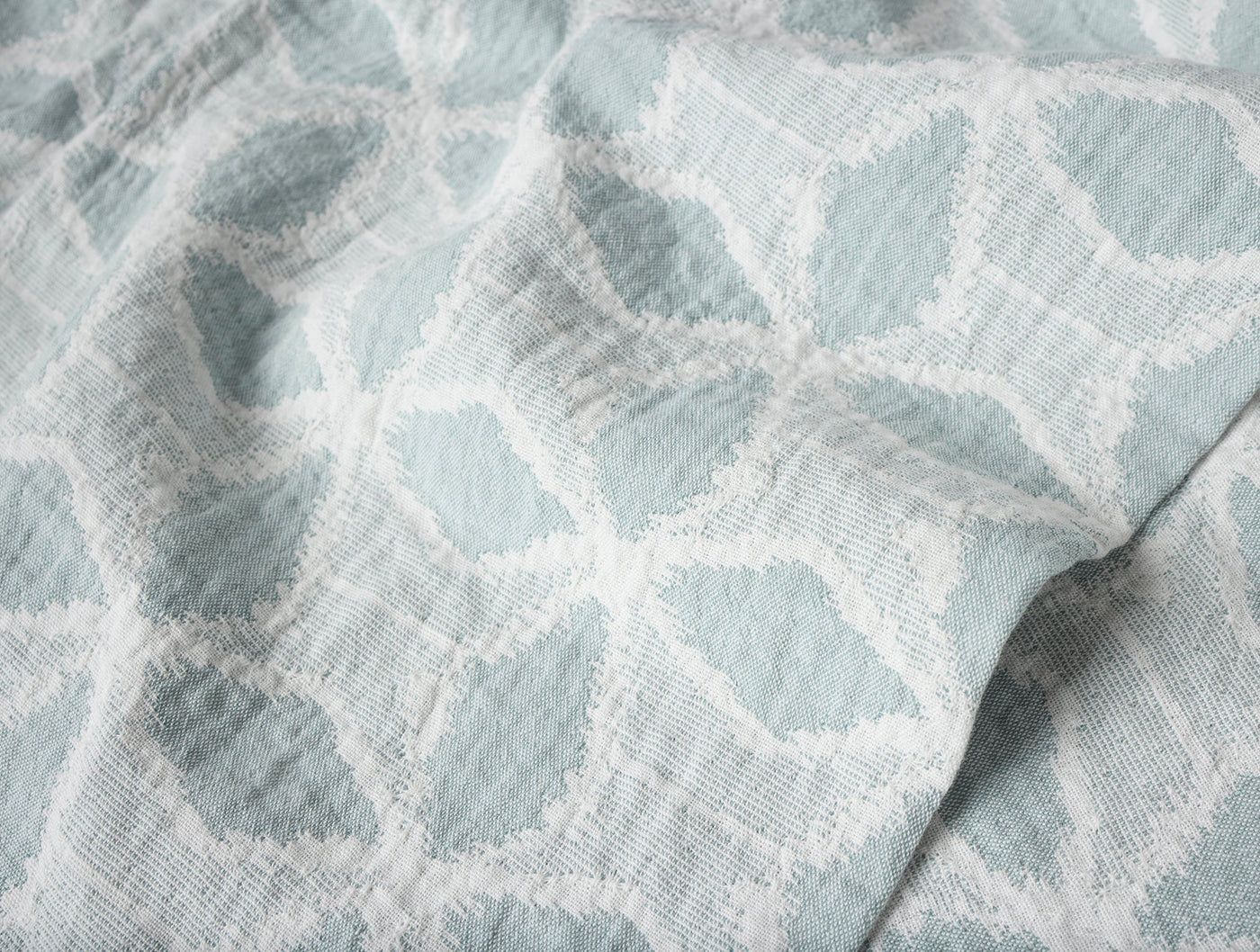 Close-up of Coyuchi Palomar throw's woven geometric floral pattern in seafoam and white.
