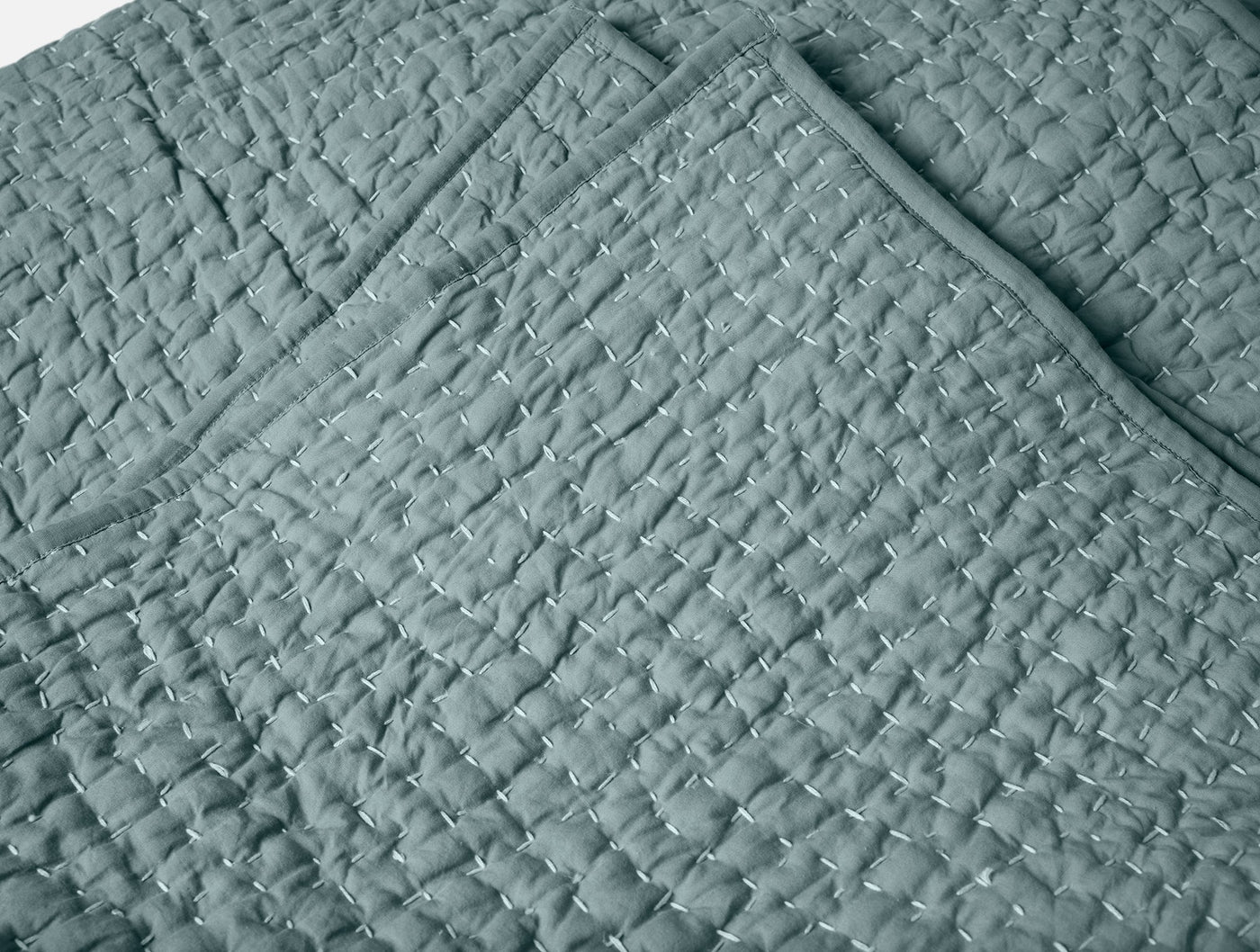 Close-up of Coyuchi Pebbled Handstitched quilt corner, showing slate blue quilted texture and stitching detail.
