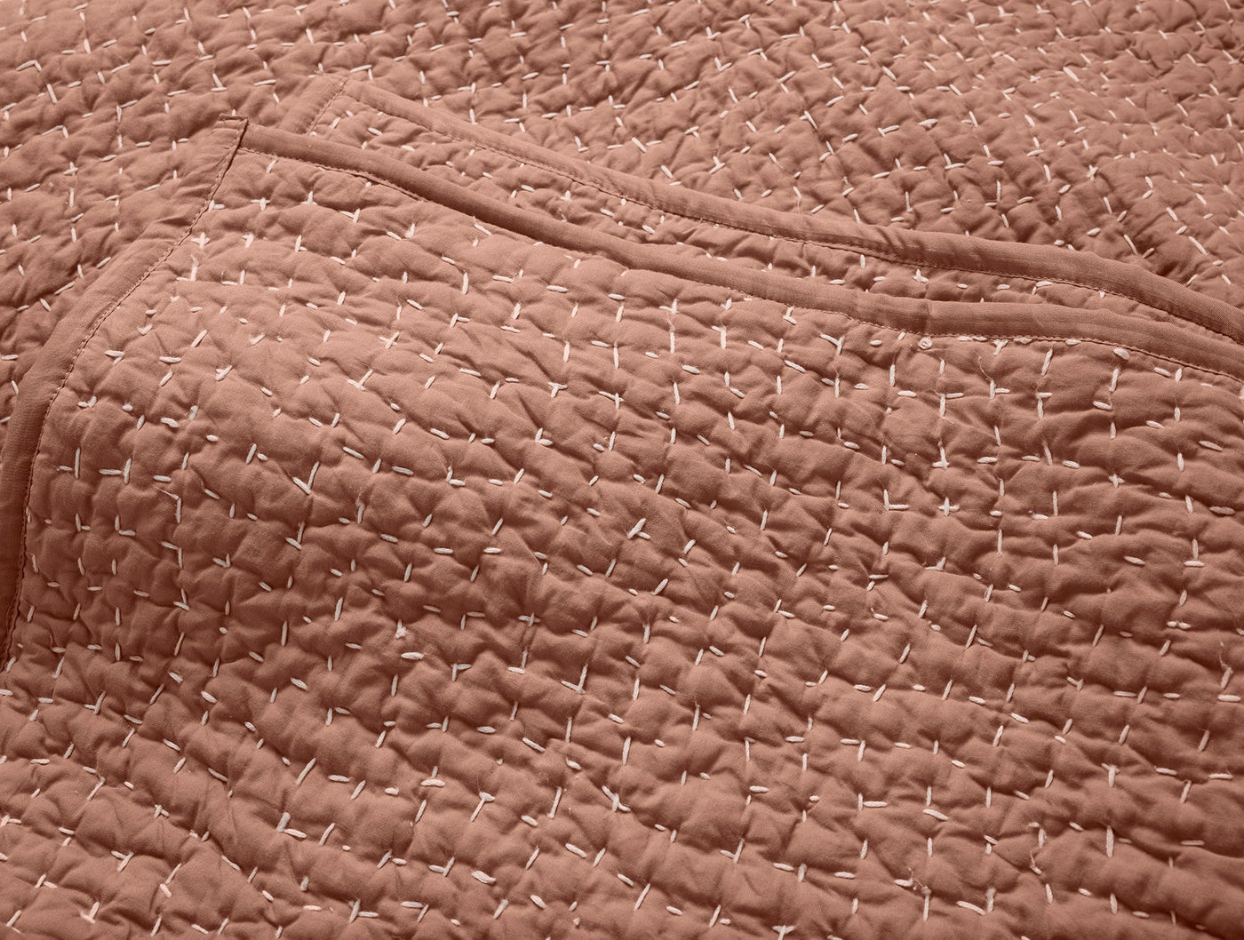 Close-up of dusty rose quilted texture with hand-stitched cross pattern on Coyuchi Pebbled quilt.