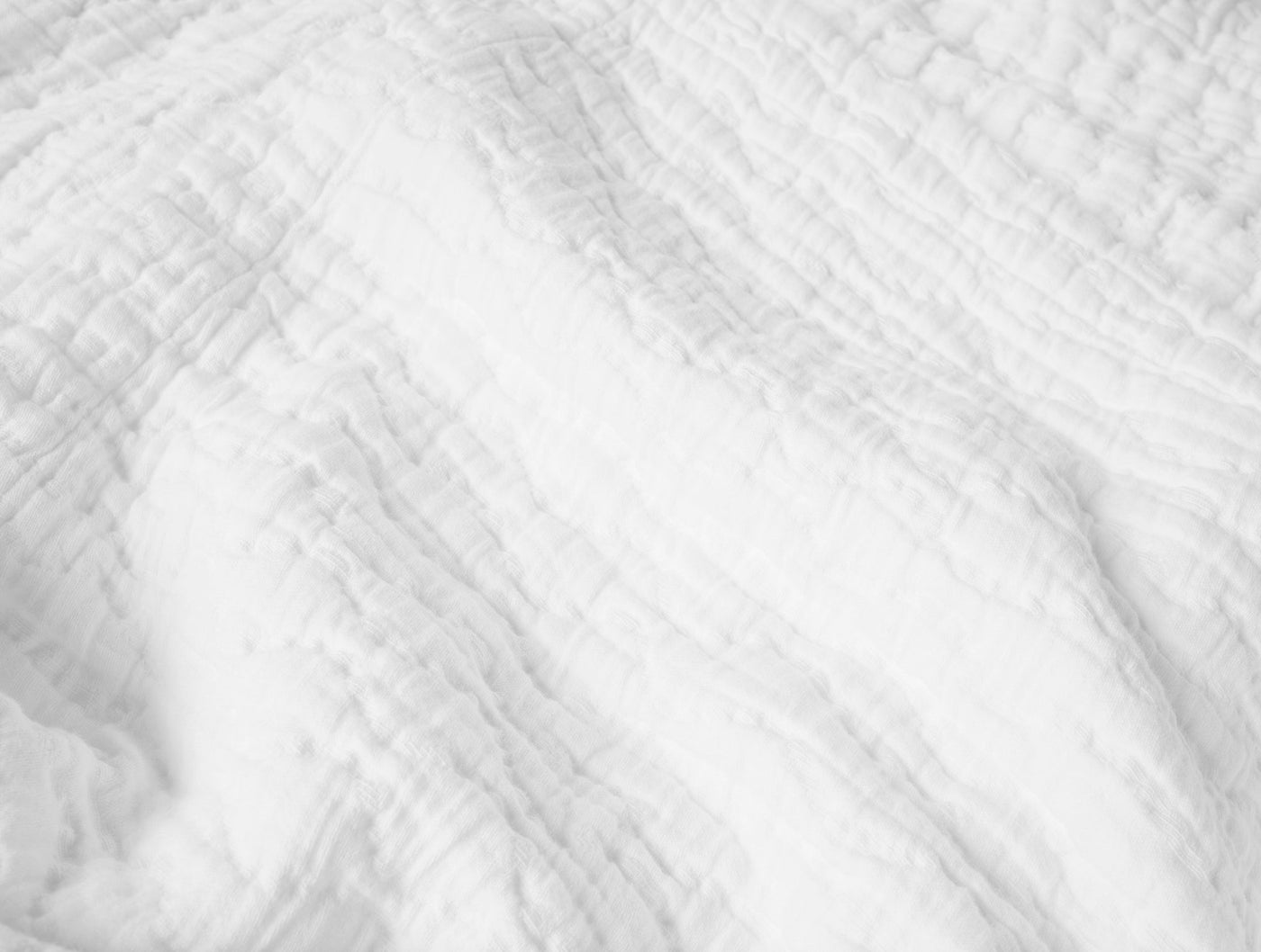 Close-up of Coyuchi Pescadero Matelasse blanket in white, showing textured crinkled weave detail.
