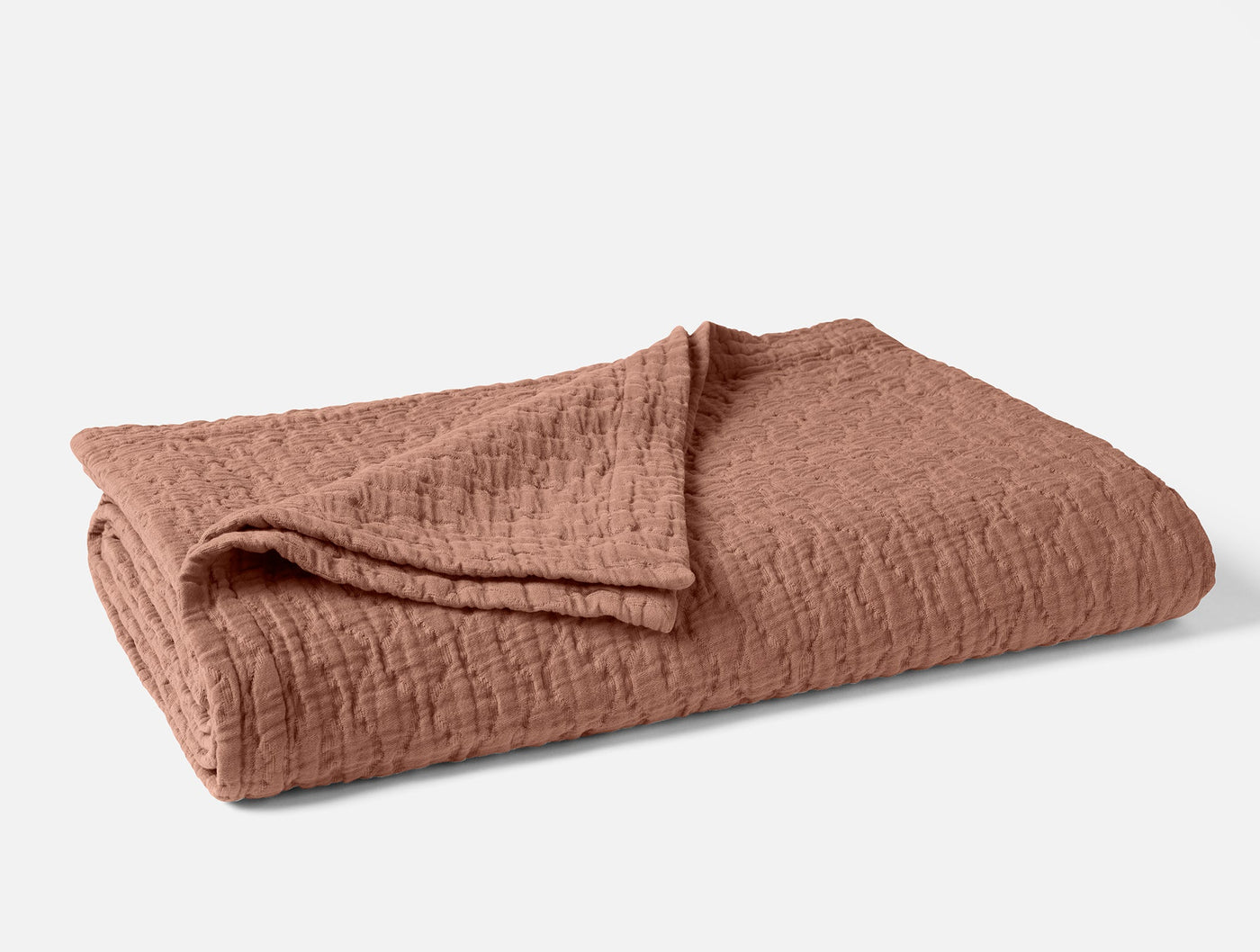 Coyuchi Pescadero Matelassé blanket folded, terracotta with textured woven surface.